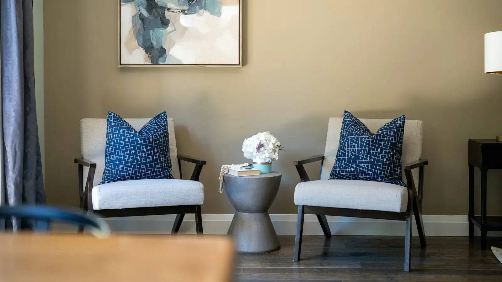 Duas poltronas com almofadas, mesa de apoio e luminária em uma sala clara.