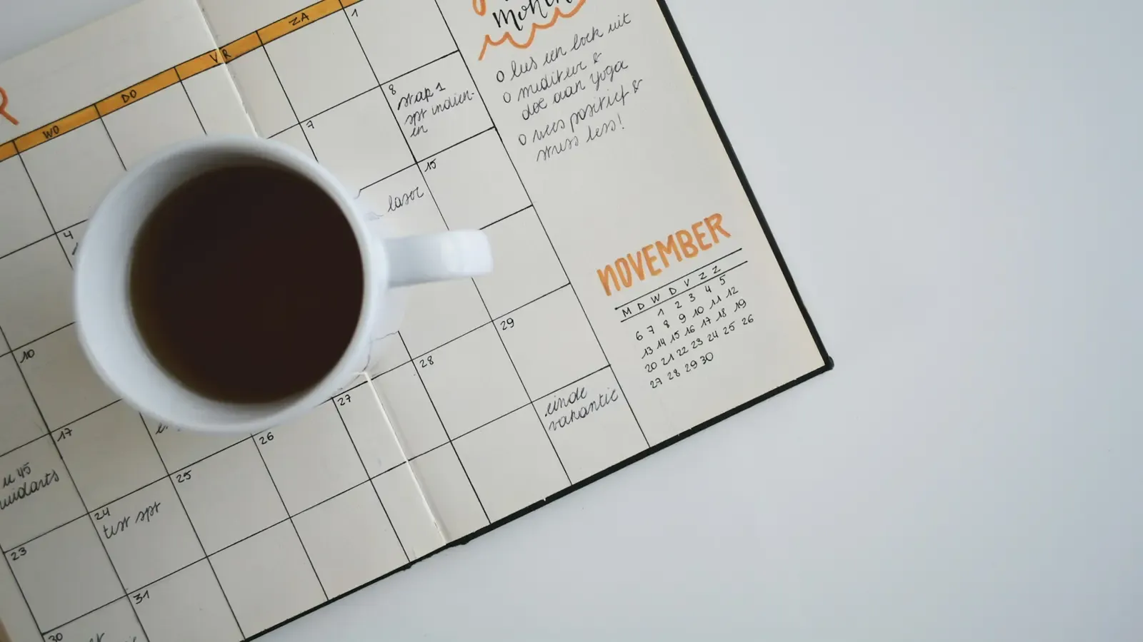 Xícara de café apoiada sobre um planner mensal aberto, com metas anotadas à mão.